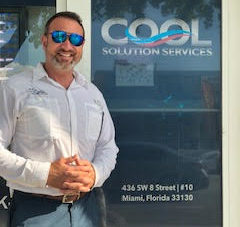 A person in white shirt and blue sunshades stands in front of COOL Solution Services office